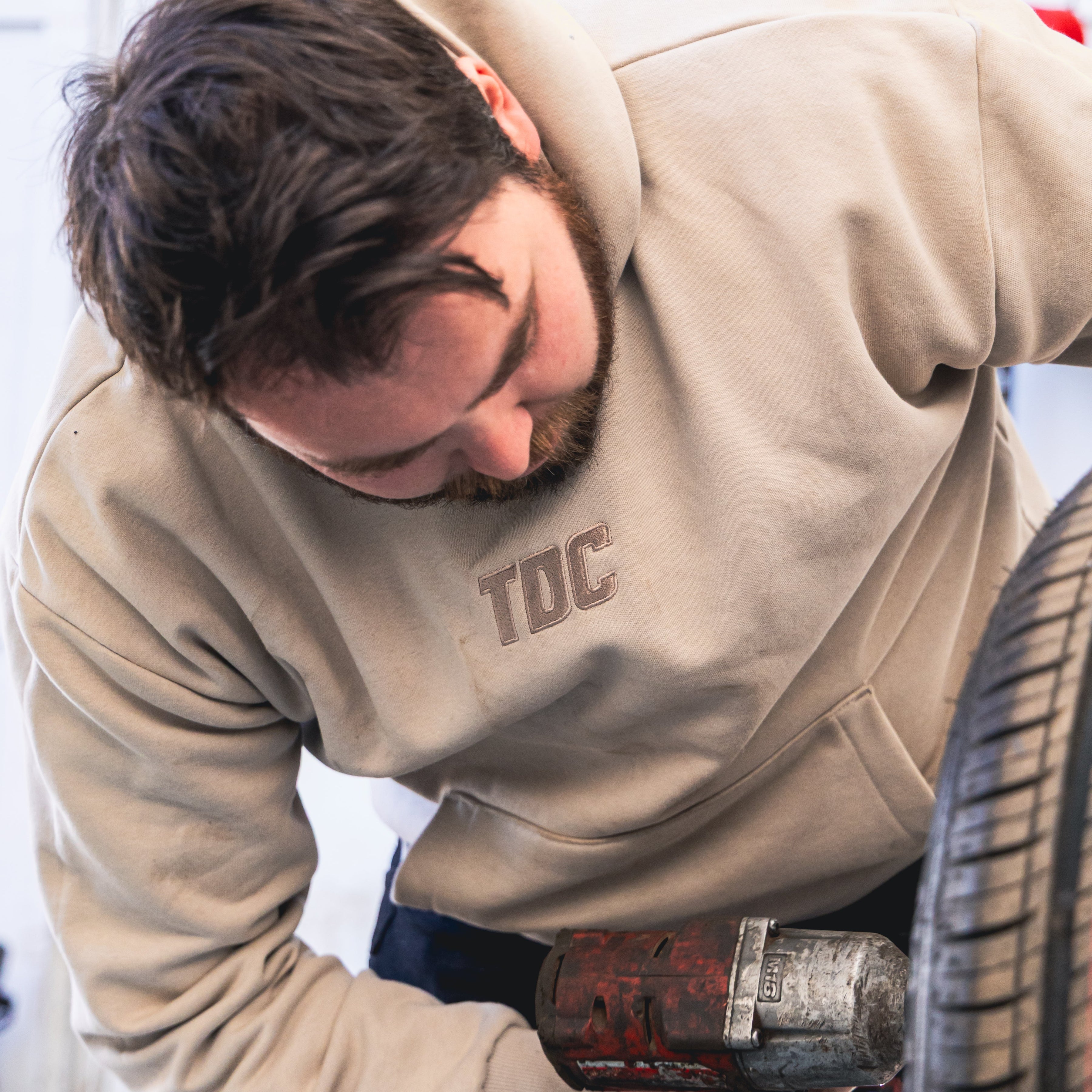 Man in a beige hoodie using a tire inflator on a tire.