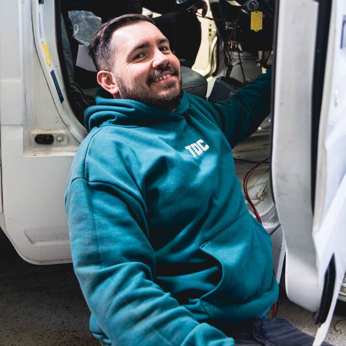 Man in a blue hoodie sitting inside a vehicle with another person in the driver's seat.