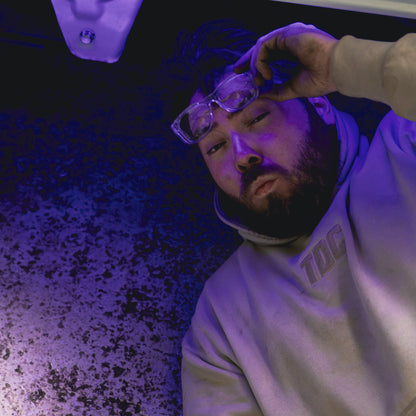 Person wearing glasses and a hoodie with text, under a purple light